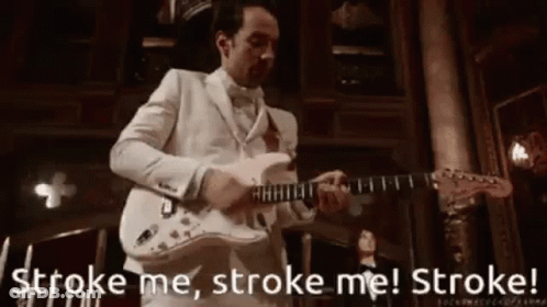 A Man In A White Suit Is Playing A Guitar In A Room . GIF