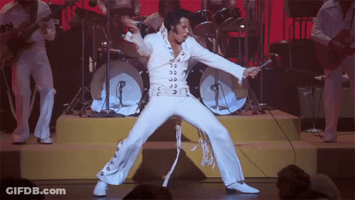 A Man In A White Suit Is Singing Into A Microphone On A Stage GIF
