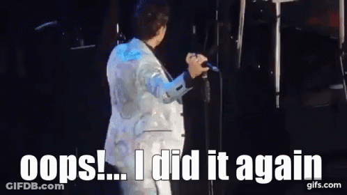 A Man In A White Suit Is Singing Into A Microphone On A Stage And Says Oops ! I Did It Again . GIF
