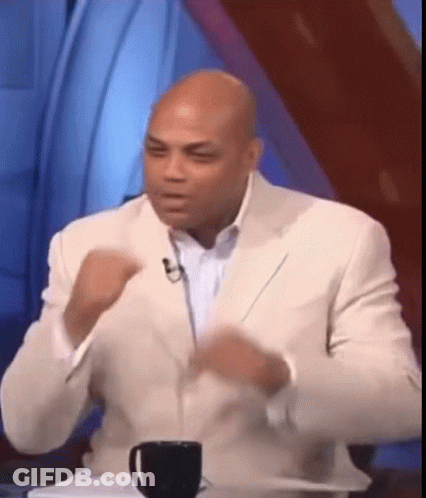 A Man In A White Suit Is Sitting At A Table With A Cup Of Coffee In Front Of Him GIF