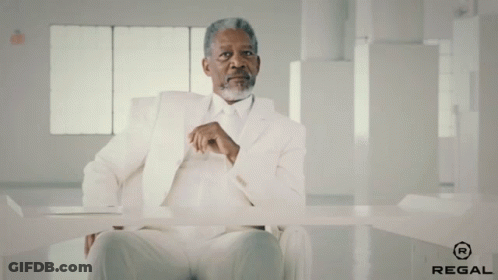A Man In A White Suit Is Sitting At A Table With Regal Written On The Bottom GIF