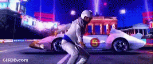 A Man In A White Suit Is Squatting In Front Of A Race Car With The Letter S On The Side . GIF