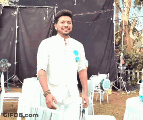 A Man In A White Suit Is Standing In Front Of A Black Backdrop GIF