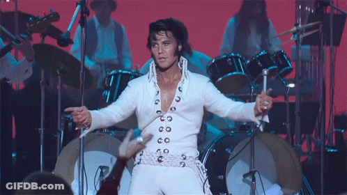 A Man In A White Suit Is Standing In Front Of A Drum Set On A Stage GIF
