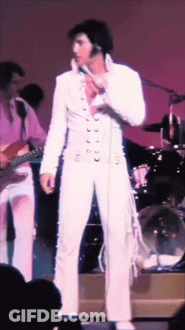 A Man In A White Suit Is Standing In Front Of A Microphone GIF
