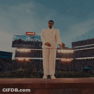 A Man In A White Suit Stands In A Crowd Of People GIF