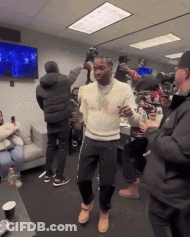 A Man In A White Sweater Is Dancing In A Room With People GIF
