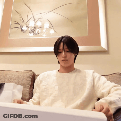 A Man In A White Sweater Is Sitting On A Couch In Front Of A Picture GIF