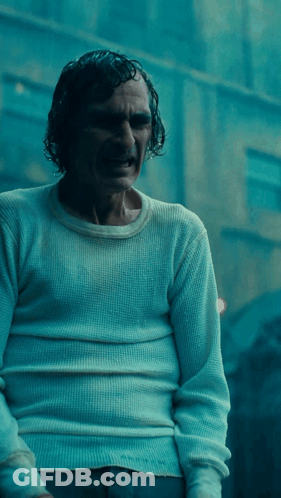 A Man In A White Sweater Is Standing In A Dark Room GIF