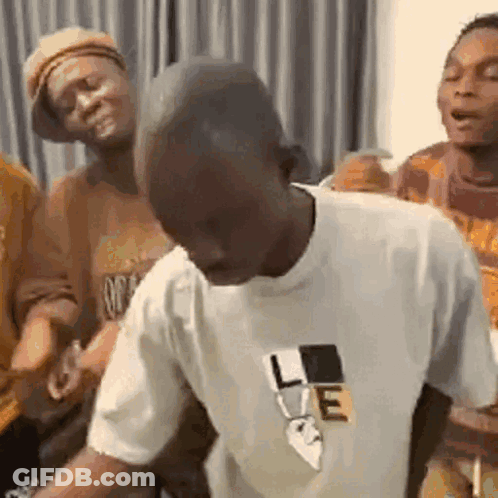 A Man In A White T-Shirt Is Dancing In A Room With Other People . GIF