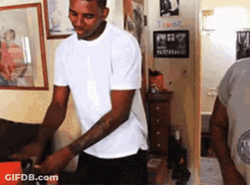 A Man In A White T-Shirt Is Kneeling Down In A Room GIF