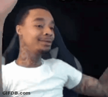 A Man In A White T-Shirt Is Sitting In A Chair With His Arms Outstretched And Smiling . GIF