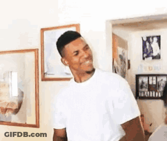 A Man In A White T-Shirt Is Standing In A Living Room With A Smile On His Face . GIF