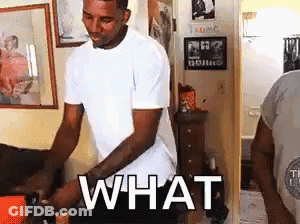 A Man In A White T-Shirt Is Standing In A Living Room With The Word What Written On His Chest . GIF