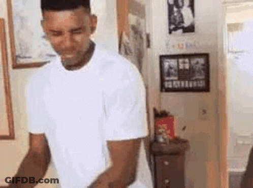 A Man In A White T-Shirt Is Standing In A Room . GIF