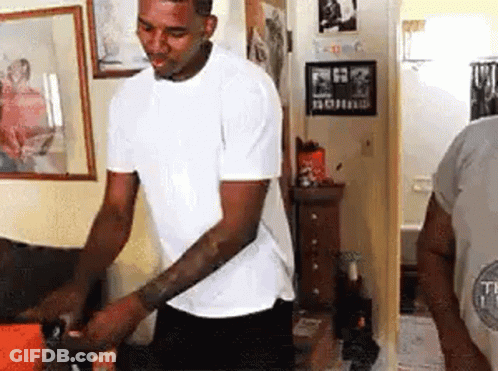 A Man In A White T-Shirt Is Standing In A Room . GIF
