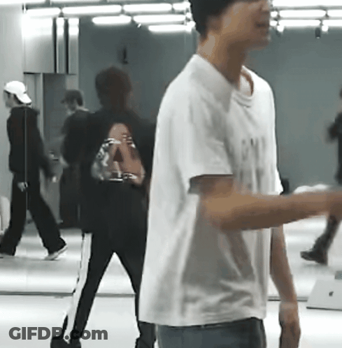 A Man In A White T-Shirt Is Standing In Front Of A Mirror In A Room . GIF