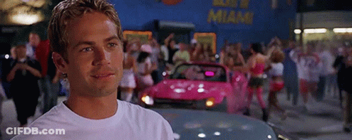 A Man In A White T-Shirt Is Standing In Front Of A Pink Car . GIF