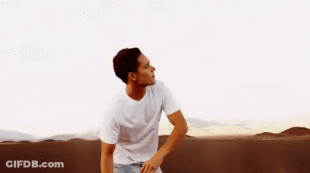 A Man In A White T-Shirt Is Standing In The Middle Of A Desert . GIF