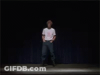 A Man In A White T-Shirt Is Standing On A Stage GIF