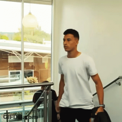 A Man In A White T-Shirt Is Walking Down Stairs GIF