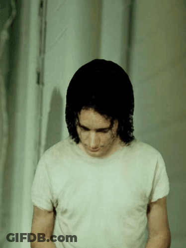 A Man In A White T-Shirt Looks Down At Something GIF