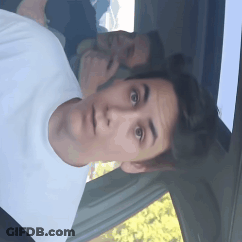 A Man In A White T-Shirt Looks Surprised In A Car GIF