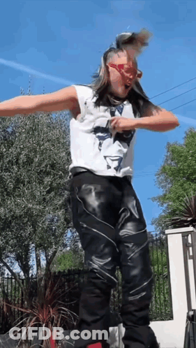 A Man In A White Tank Top And Black Leather Pants Is Jumping In The Air GIF