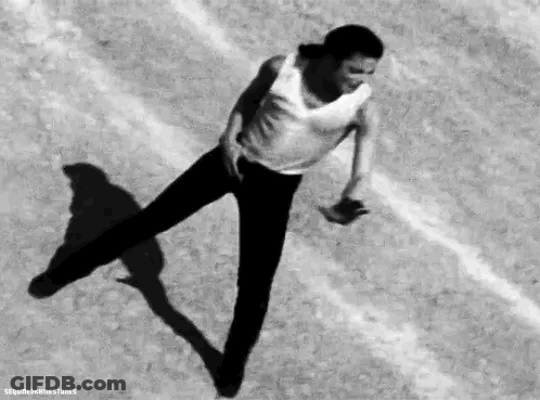 A Man In A White Tank Top And Black Pants Is Dancing On A Track . GIF