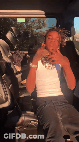 A Man In A White Tank Top And Black Pants Is Sitting In The Back Seat Of A Car GIF