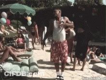 A Man In A White Tank Top And Red Shorts Is Dancing In Front Of A Group Of People GIF