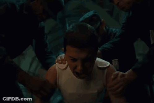 A Man In A White Tank Top Is Being Helped By Two Men . GIF
