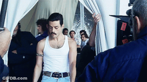 A Man In A White Tank Top Is Being Photographed By A Man In A Blue Shirt GIF