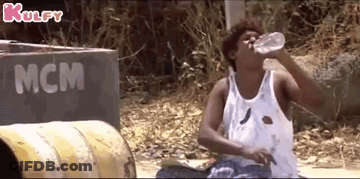 A Man In A White Tank Top Is Drinking Water From A Bottle . GIF