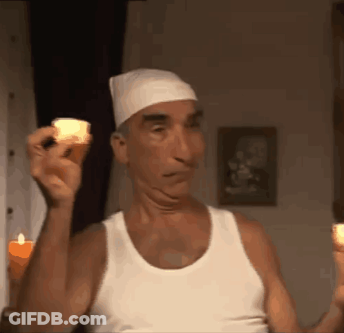 A Man In A White Tank Top Is Holding Two Lit Candles GIF