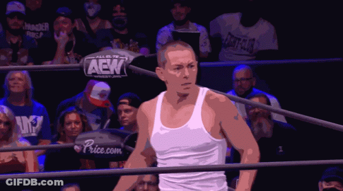 A Man In A White Tank Top Is In A Wrestling Ring With A Sign That Says Aek On It GIF