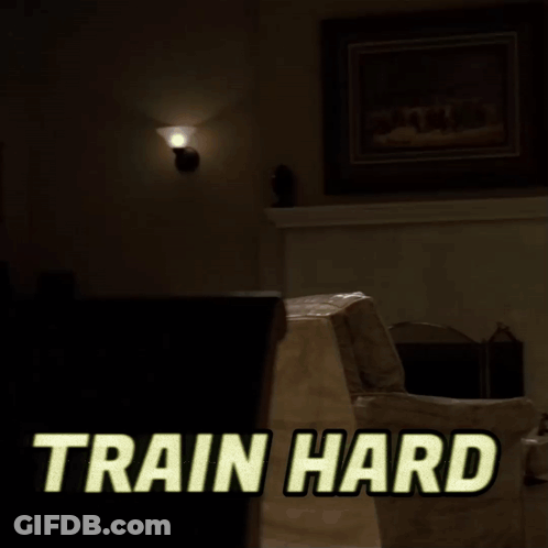 A Man In A White Tank Top Is Lifting A Dumbbell With The Words Train Hard Written Above Him GIF