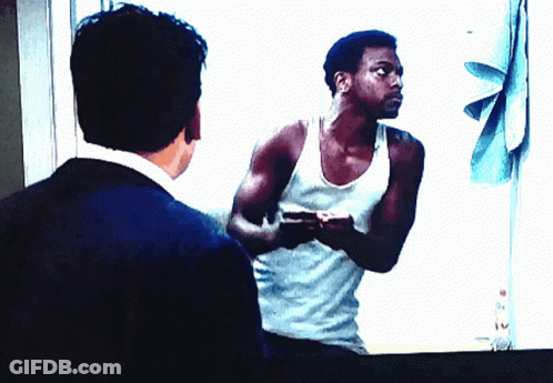 A Man In A White Tank Top Is Looking At His Reflection In A Mirror GIF