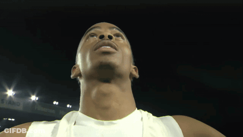 A Man In A White Tank Top Is Looking Up At The Camera GIF