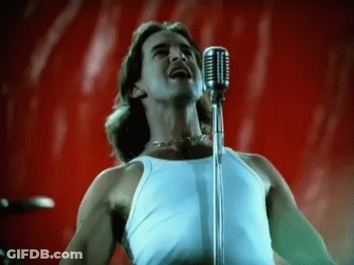 A Man In A White Tank Top Is Singing Into A Microphone On A Red Background . GIF