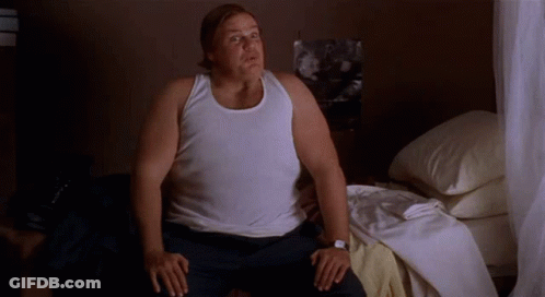 A Man In A White Tank Top Is Sitting On A Bed . GIF