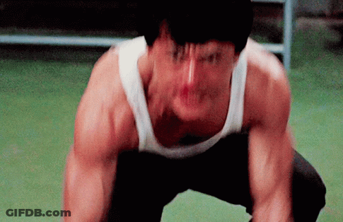 A Man In A White Tank Top Is Squatting Down And Making A Funny Face GIF