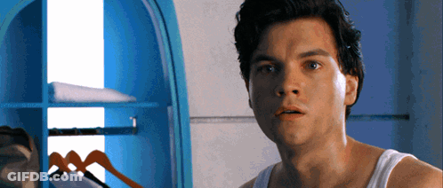 A Man In A White Tank Top Is Standing In Front Of A Closet GIF