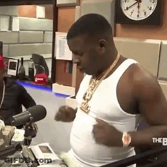 A Man In A White Tank Top Is Standing In Front Of A Microphone In A Room . GIF