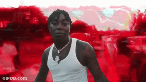 A Man In A White Tank Top Is Standing In Front Of A Red And White Background . GIF