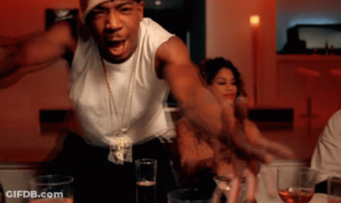 A Man In A White Tank Top Is Standing In Front Of A Table With Glasses Of Beer GIF