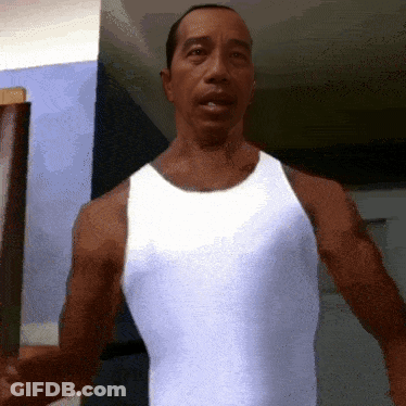 A Man In A White Tank Top Is Standing In Front Of A Wall GIF
