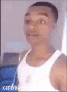 A Man In A White Tank Top Is Standing In Front Of A Window And Looking At The Camera . GIF