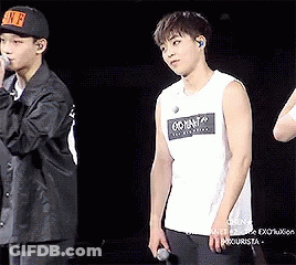 A Man In A White Tank Top Is Standing Next To Another Man In A Black Jacket . GIF