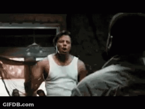 A Man In A White Tank Top Is Standing Next To Another Man In A Room . GIF